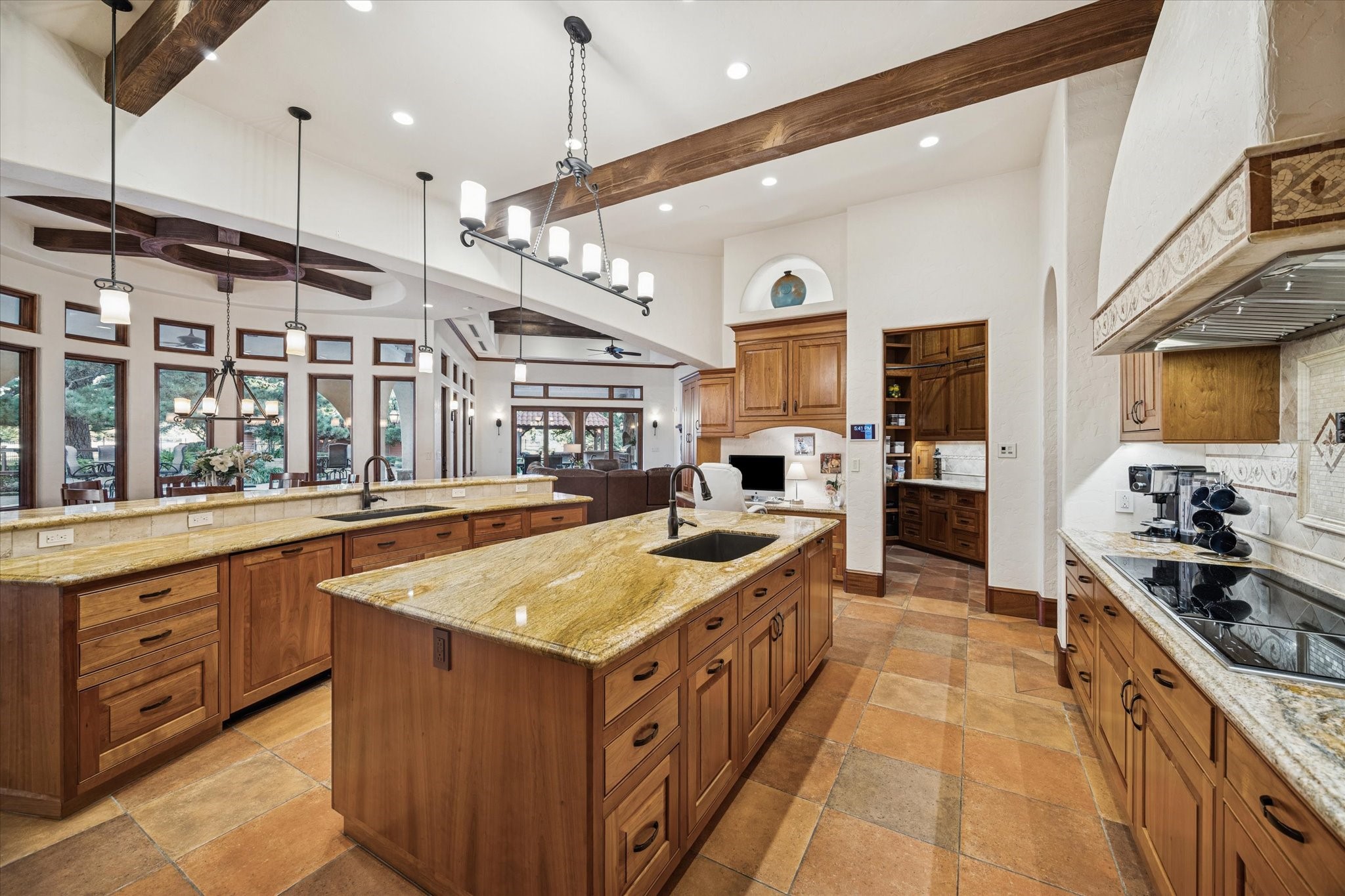 21538 Mueschke Road Tomball, TX 77377 - Photo 15 of 50 Beautifully illuminated kitchen featuring recessed lighting, elegant pendants, niche accents, and under-cabinet illumination that create a warm, inviting ambiance and highlight the rich finishes throughout. A convenient chef’s desk adds functionality, while a discreet sliding door reveals a spacious walk-in pantry with granite counter space for prep or mixing spices, custom shelving, cabinetry, and an iconic Putnam rolling ladder, combining practicality with timeless elegance.