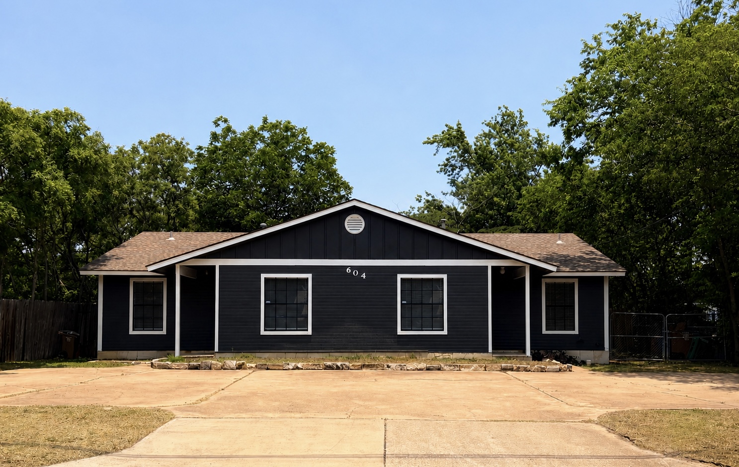 A well-maintained single-story dwelling with dark siding and a spacious concrete driveway.