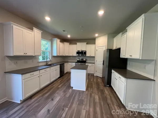 a kitchen with granite countertop a refrigerator a sink dishwasher and a stove top oven with wooden floor