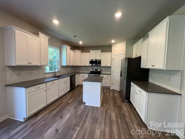 a kitchen with granite countertop a refrigerator a sink dishwasher and a stove top oven with wooden floor