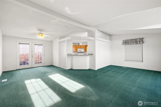 a view of an empty room with window and kitchen view