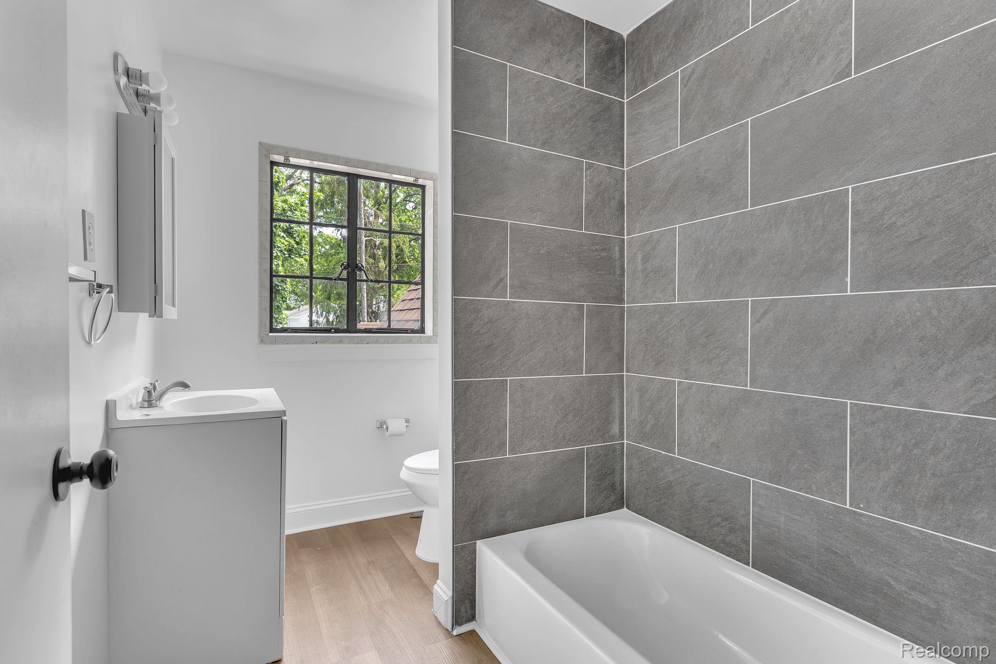 19510 Stratford Road Detroit, MI 48221 - Photo 34 of 45 Bathroom featuring a tub with large format gray tile surround, white vanity with integrated sink, and wood-finish flooring
