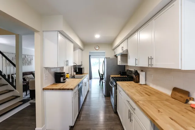 a kitchen with stainless steel appliances a stove a sink a refrigerator white cabinets and couches with wooden floor