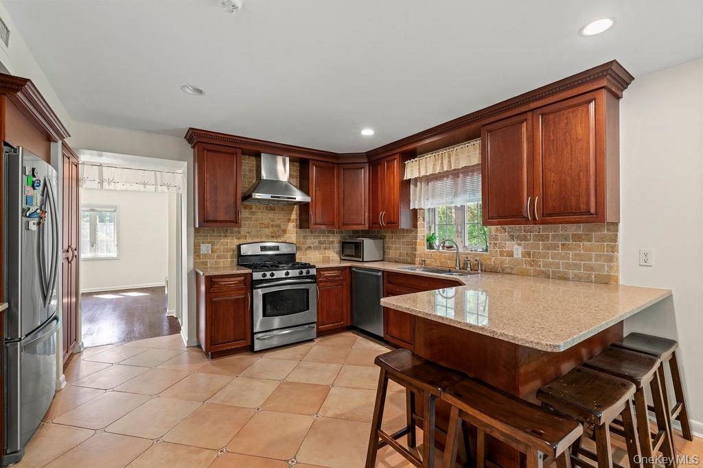 60 Plymouth Road Great Neck, NY 11023 - Photo 14 of 36 Kitchen featuring appliances with stainless steel finishes, tasteful backsplash, a peninsula, a breakfast bar, and light tile patterned floors