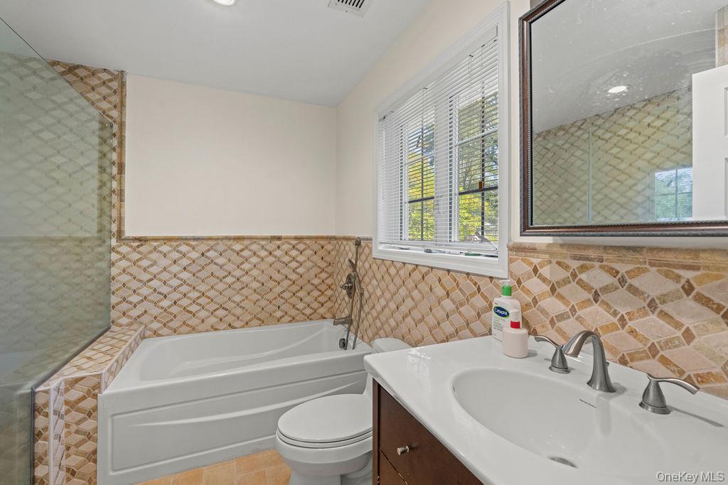 60 Plymouth Road Great Neck, NY 11023 - Photo 25 of 36 Bathroom featuring a bath, vanity, tile walls, light tile patterned flooring, and a wainscoted wall
