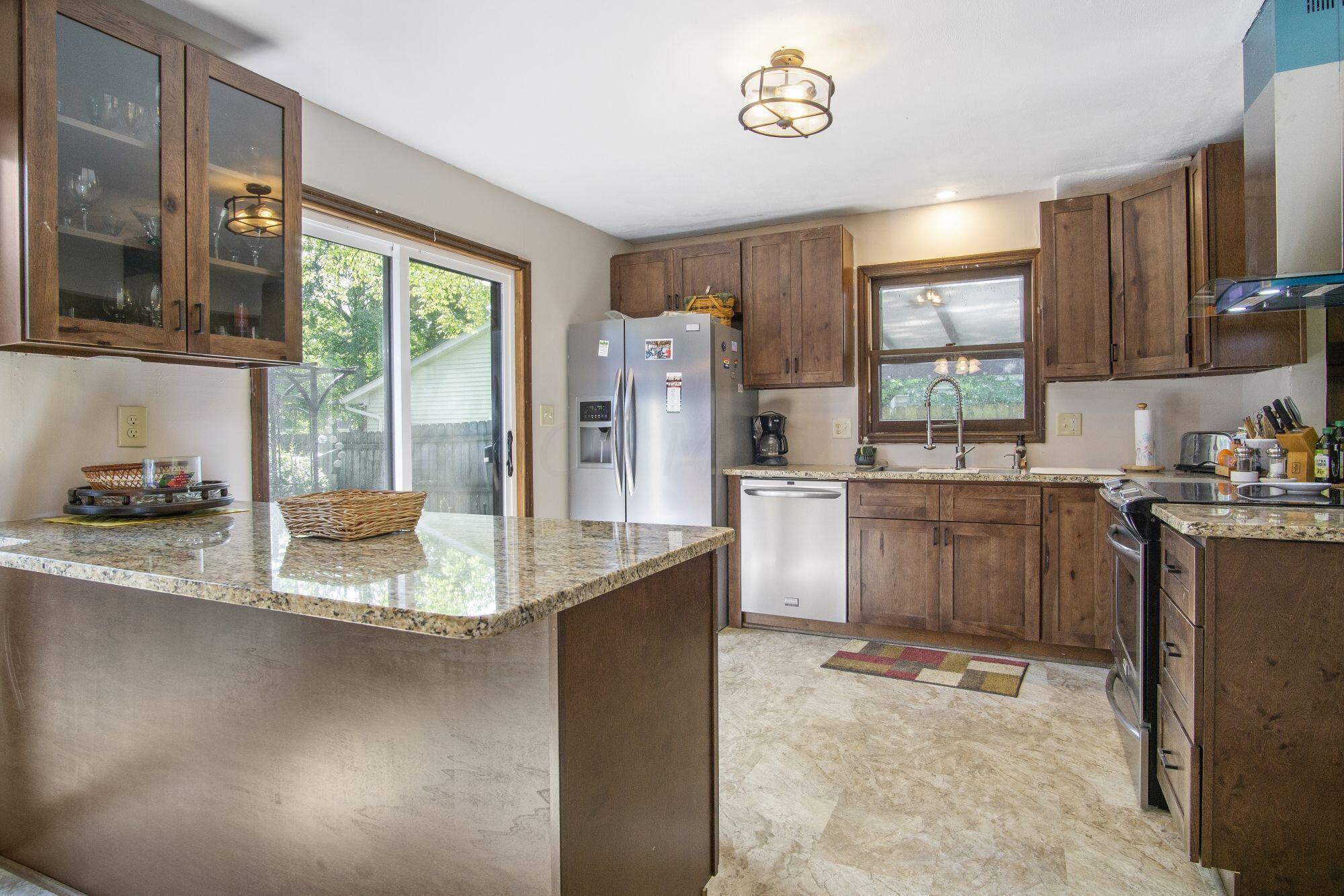 6053 Rocky Rill Road Columbus, OH 43235 - Photo 13 of 28 New 2021 Breakfast Bar, 42" cabinets with granite counter tops. Glass front display cabinets. Light fixture. New 2019 sliding glass door opens to Court Yard.