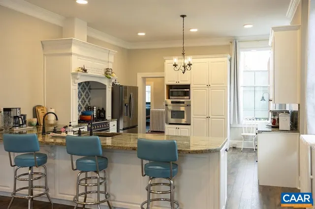 a kitchen with kitchen island granite countertop a stove a refrigerator a sink dishwasher and white cabinets with wooden floor