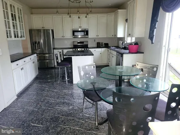 a kitchen with stainless steel appliances kitchen island granite countertop a stove a refrigerator a sink a dining table and chairs