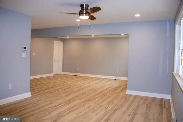 an empty room with wooden floor ceiling fan and windows
