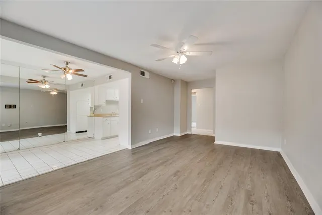 a view of an empty room with wooden floor and a ceiling fan