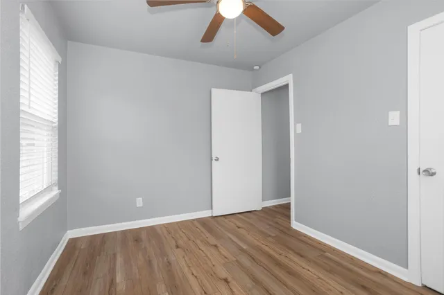 an empty room with wooden floor fan and windows