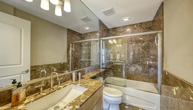 a bathroom with a granite countertop sink a toilet a mirror and shower