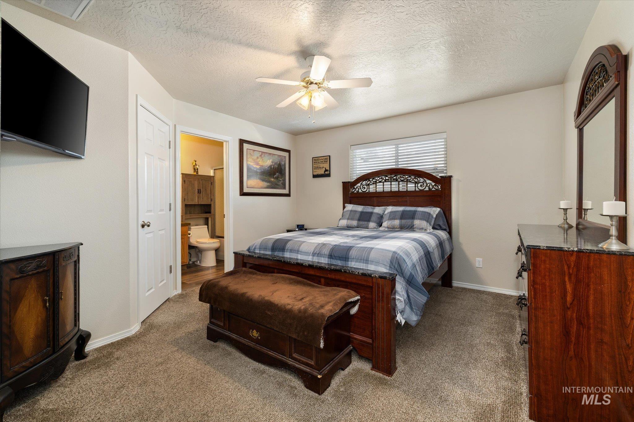 5401 Barkley Way Caldwell, ID 83607 - Photo 11 of 35 Carpeted bedroom featuring a ceiling fan with integrated lighting, a window with blinds, and an attached three-piece bathroom with wood-finish cabinetry