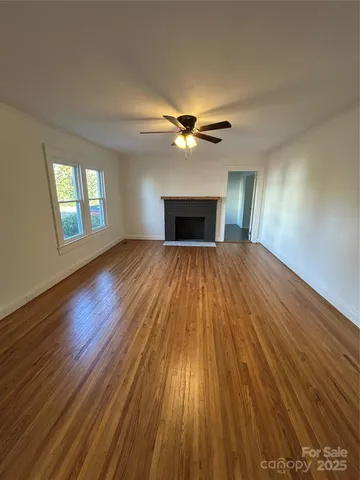 a view of an empty room with wooden floor fireplace and a window