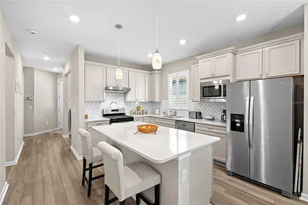 a kitchen with stainless steel appliances a refrigerator a stove a sink a dining table and chairs with wooden floor