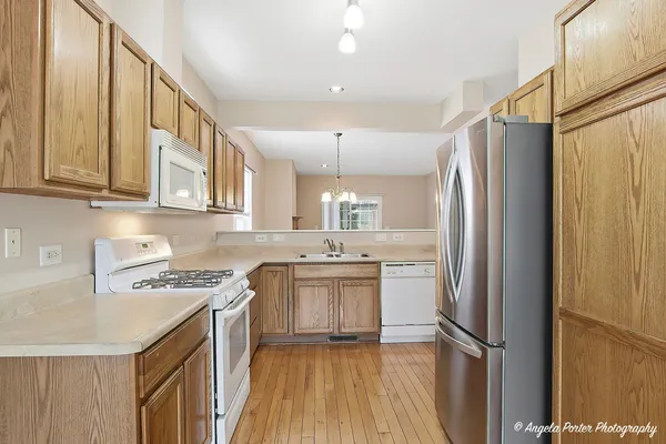a kitchen with stainless steel appliances granite countertop a refrigerator a sink dishwasher a stove and a dining table with wooden floor