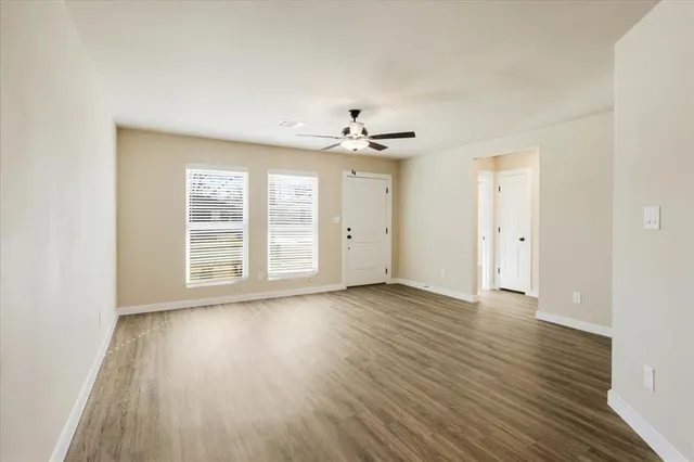 an empty room with wooden floor chandelier fan and windows