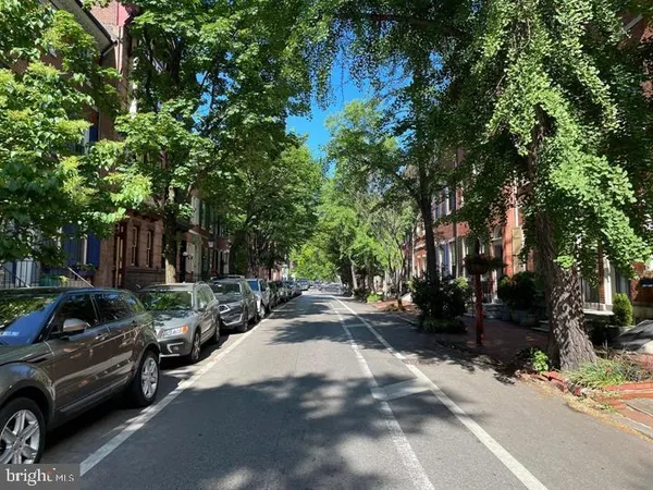 a sidewalk with trees and wooden fence