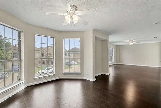 a view of an empty room with wooden floor and a ceiling fan