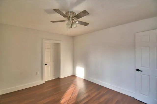 a view of an empty room with wooden floor and a ceiling fan