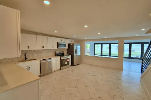 a large kitchen with stainless steel appliances granite countertop a large counter top a stove a refrigerator a sink and a microwave