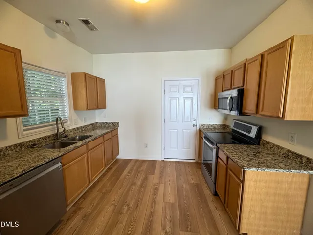 a kitchen with granite countertop a sink wooden floor and stainless steel appliances