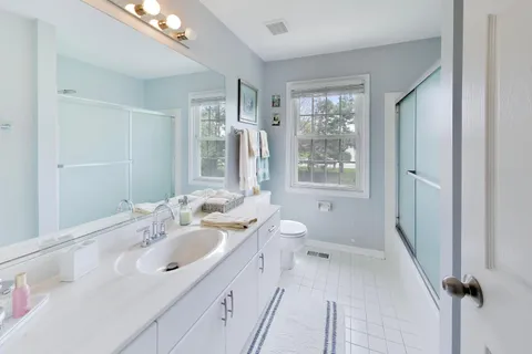a bathroom with a double vanity sink toilet mirror and windows