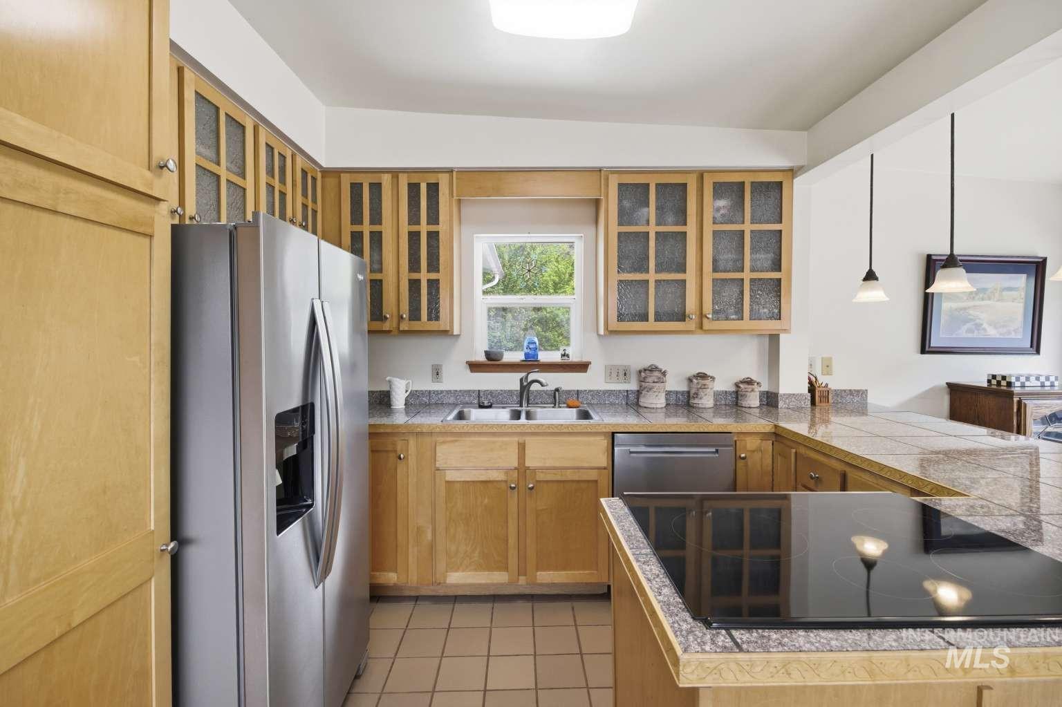901 Main Street Kendrick, ID 83537 - Photo 17 of 50 Kitchen featuring light wood cabinetry with glass-front upper doors, stainless steel appliances, a built-in cooktop, and tile countertops
