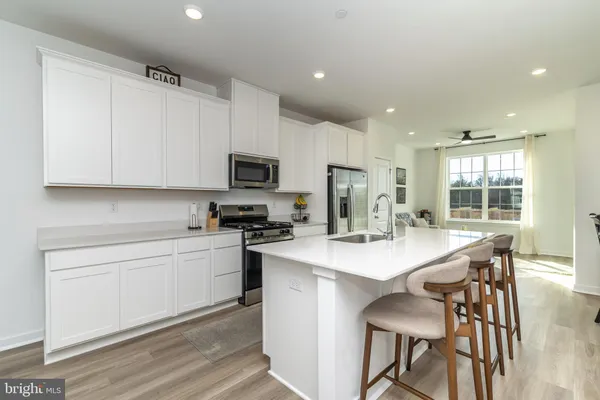 a kitchen with stainless steel appliances a stove a sink a microwave a refrigerator and white cabinets with wooden floor