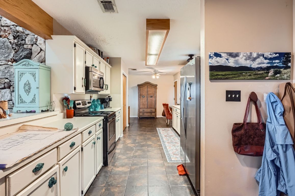 760 Skyline Ridge Lookout Wimberley, TX 78676 - Photo 11 of 40 Kitchen featuring appliances with stainless steel finishes, white cabinetry, light countertops, stone finish floors, and a ceiling fan