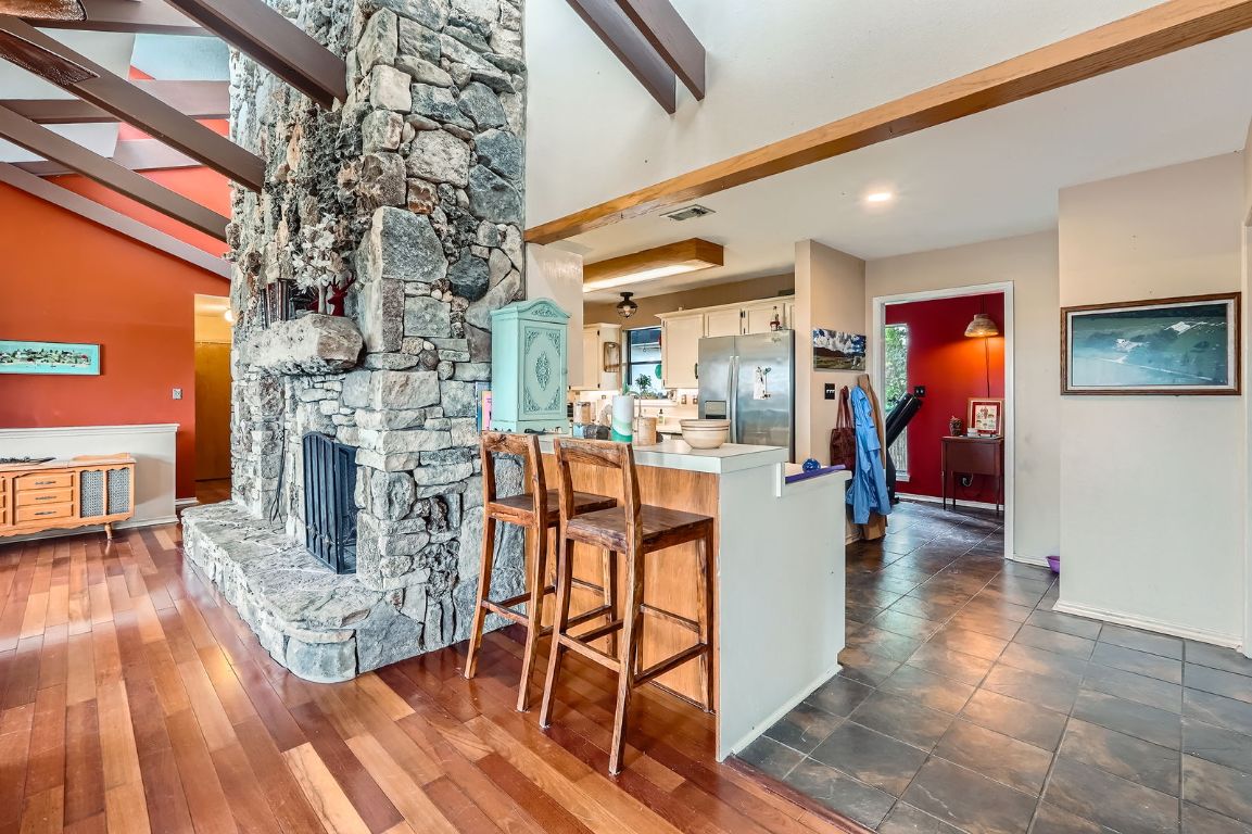 760 Skyline Ridge Lookout Wimberley, TX 78676 - Photo 5 of 40 Kitchen with stainless steel fridge, a breakfast bar, a peninsula, white cabinets, and a stone fireplace