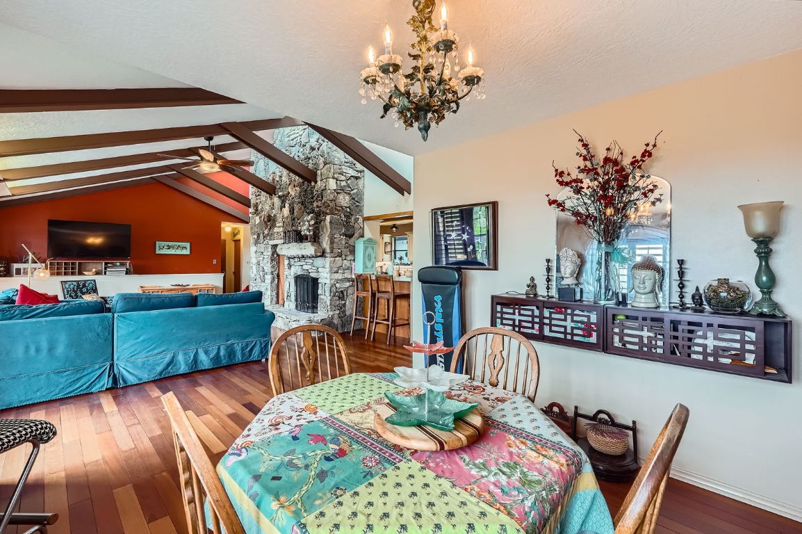 760 Skyline Ridge Lookout Wimberley, TX 78676 - Photo 9 of 40 Dining space featuring wood finished floors, a stone fireplace, a chandelier, and a ceiling fan