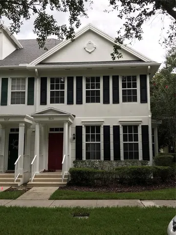 a view of a white house with large windows and a yard with plants and large trees