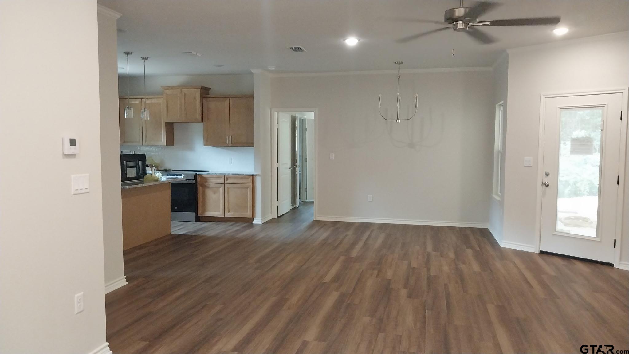 1262 George Richey Road Gladewater, TX 75647 - Photo 5 of 22 an empty room with wooden floor a ceiling fan and kitchen space