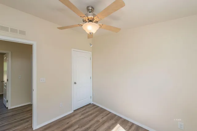 an empty room with a chandelier fan and wooden floor