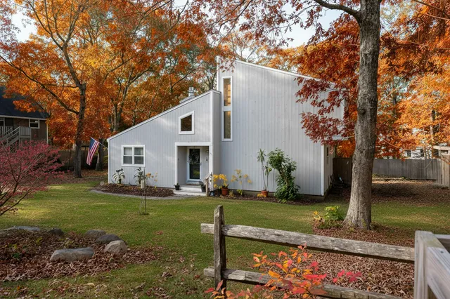 a view of a white house next to a yard with big trees