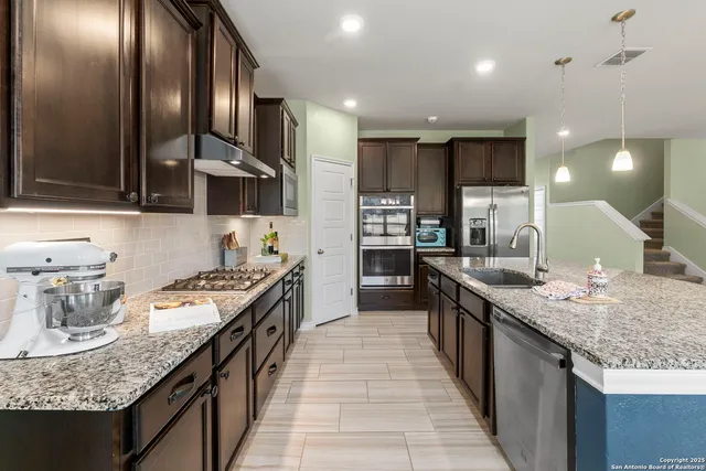 a kitchen with granite countertop kitchen island stainless steel appliances a sink stove and cabinets