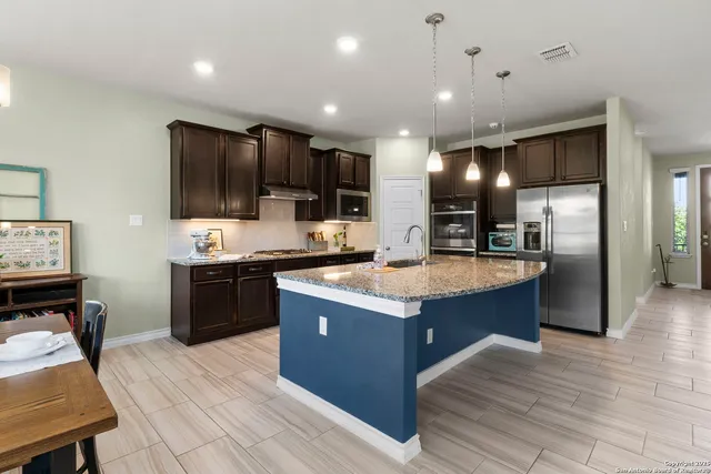 a kitchen with stainless steel appliances kitchen island granite countertop a stove top oven a sink dishwasher a refrigerator and a dining table with wooden floor