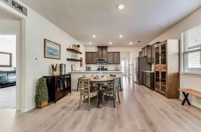 a kitchen with stainless steel appliances kitchen island granite countertop a refrigerator a stove a sink a dining table and chairs with wooden floor