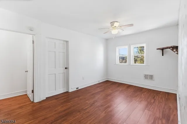 a view of an empty room with wooden floor and a ceiling fan