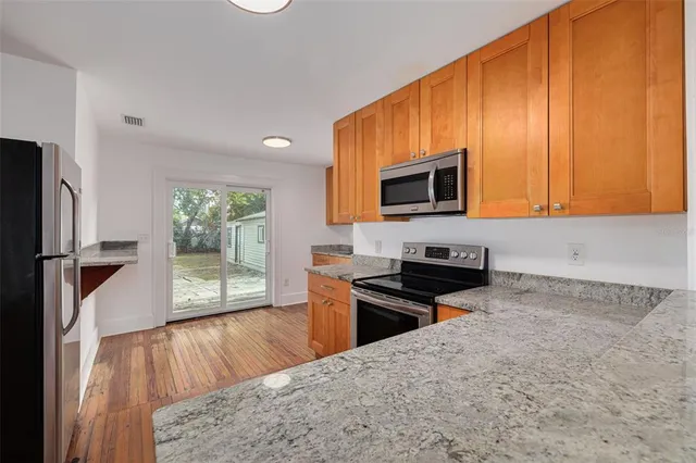 a kitchen with stainless steel appliances granite countertop a stove a sink dishwasher a microwave oven with cabinets and wooden floor