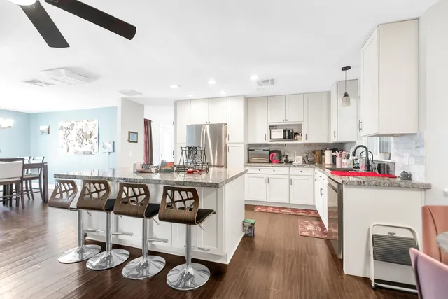 a kitchen with stainless steel appliances granite countertop a stove top oven a sink a dining table and chairs with wooden floor