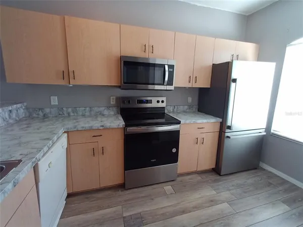 a kitchen with stainless steel appliances granite countertop white cabinets a sink a window and wooden floor
