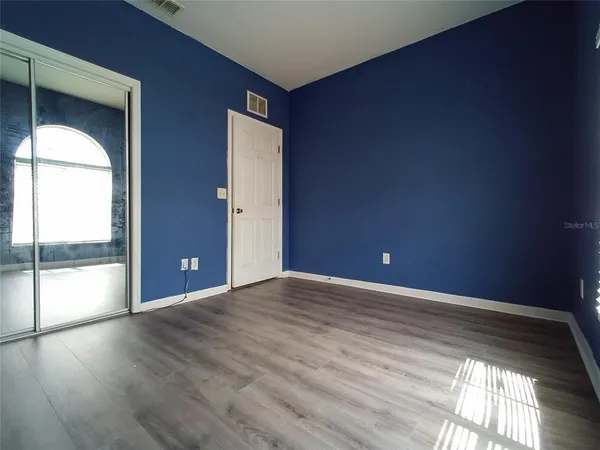 a view of an empty room with wooden floor and a kitchen