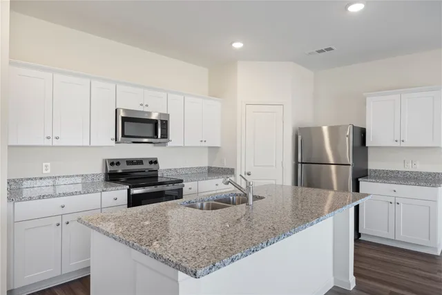 a kitchen with kitchen island granite countertop a sink a stove a refrigerator and white cabinets