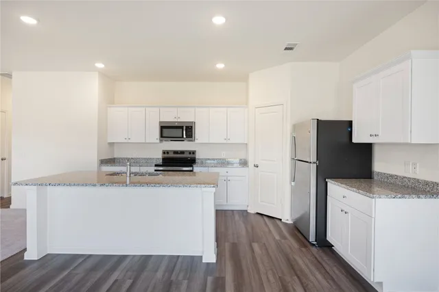 a kitchen with granite countertop a refrigerator stove a sink and white cabinets with wooden floor