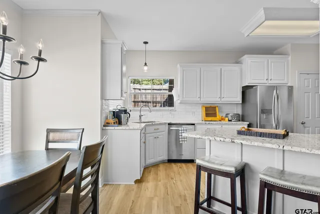 a kitchen with stainless steel appliances granite countertop a stove a refrigerator a sink dishwasher a dining table and chairs with wooden floor