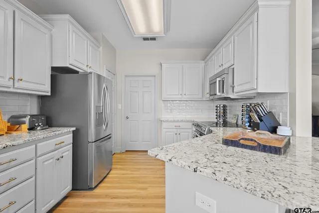a kitchen with stainless steel appliances granite countertop a refrigerator sink and white cabinets
