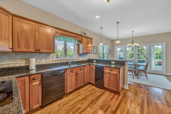 a kitchen with stainless steel appliances granite countertop wooden floors wooden cabinets a stove a sink and a large window