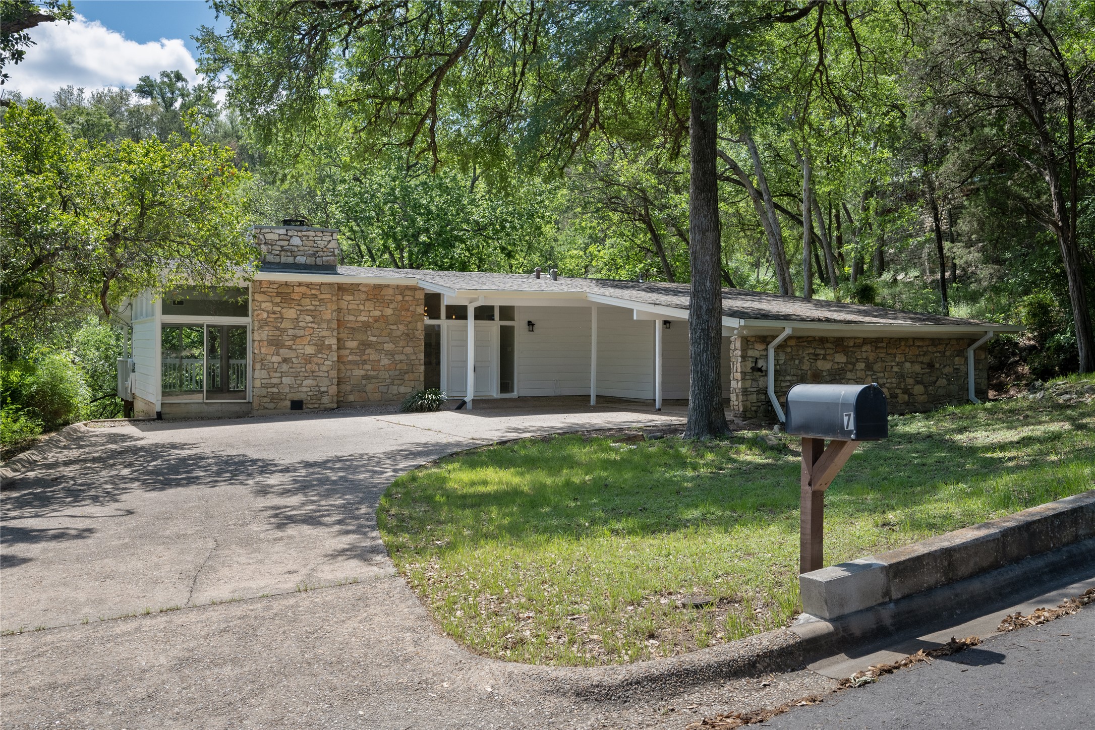 View of front facade featuring stone siding, driveway, a carport, and a front lawn